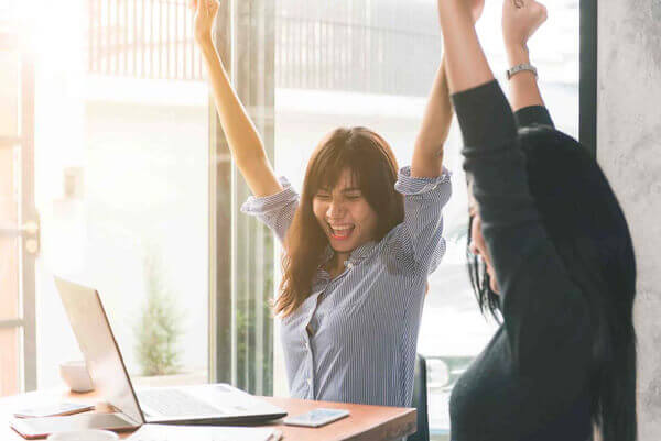 Two young business women sitting at table in cafe. Putting Hands in the air.