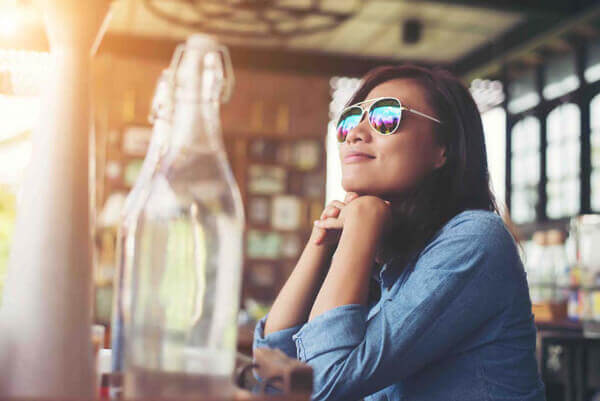 Thoughtful young hipster woman with glasses sitting at table at cafe.